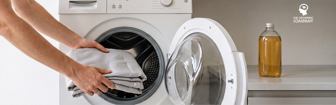 Des mains placent un drap de mise à la terre gris plié dans un lave-linge à hublot ouvert