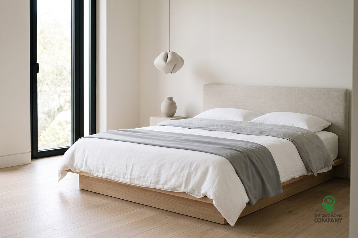 A grey earthing half sheet folded across the foot of a bed over white bedding, ready to be tucked in.