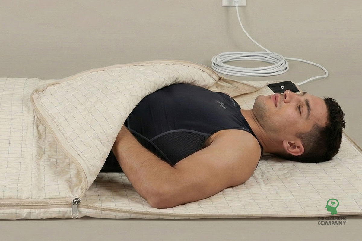 Homme allongé à l'intérieur du Grounding Recovery Sleep Bag fermé, portant un masque de sommeil, cordon branché